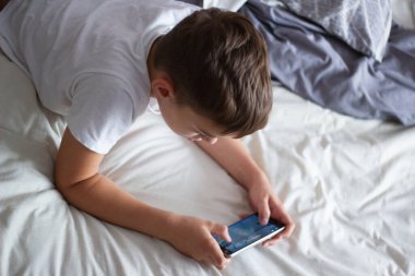 child lying in bed playing on a mobile phone