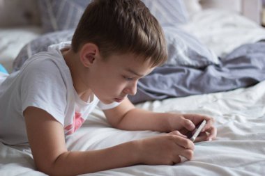 child lying in bed playing on a mobile phone