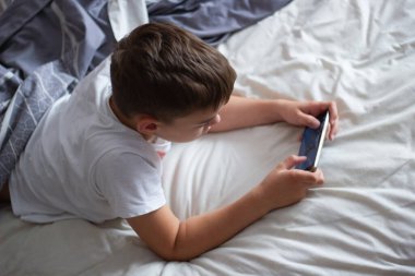 child lying in bed playing on a mobile phone