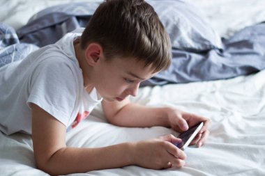 child lying in bed playing on a mobile phone