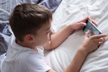 child lying in bed playing on a mobile phone