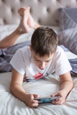 child lying in bed playing on a mobile phone