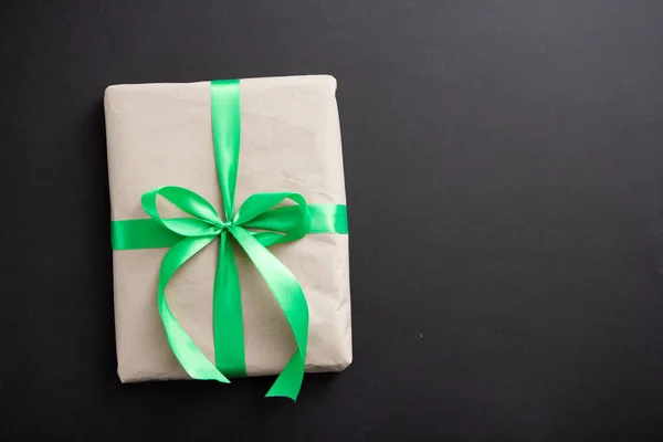 a gift in craft paper and a green ribbon on a black background with confetti