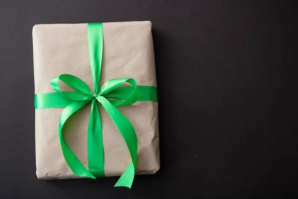 a gift in craft paper and a green ribbon on a black background with confetti