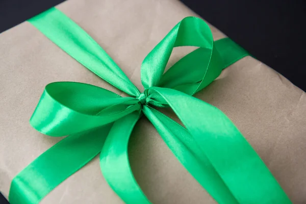 a gift in craft paper and a green ribbon on a black background with confetti