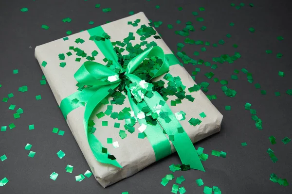 a gift in craft paper and a green ribbon on a black background with confetti