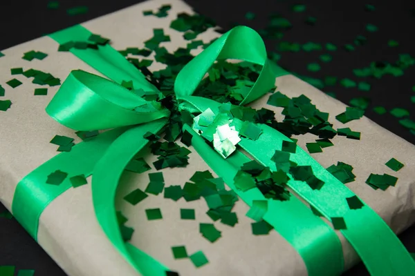 a gift in craft paper and a green ribbon on a black background with confetti