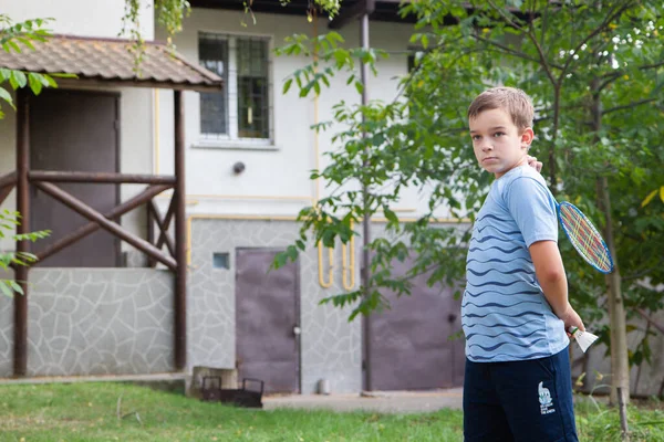 a boy with a badminton racket, a boy plays badminton on the background of the house