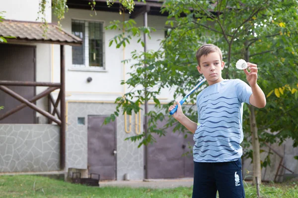 a boy with a badminton racket, a boy plays badminton on the background of the house