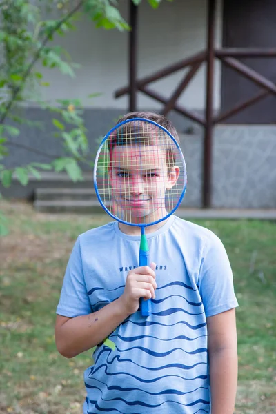 a boy with a badminton racket, a boy plays badminton on the background of the house