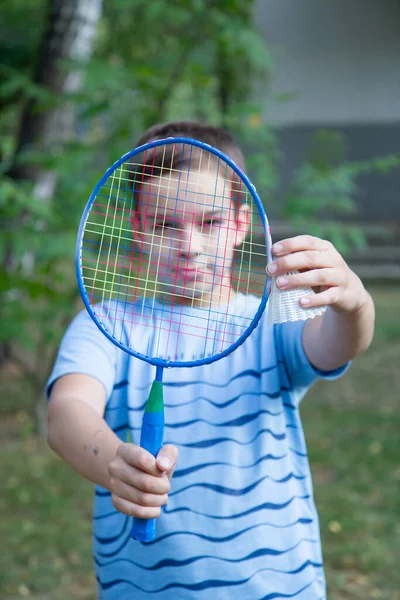 a boy with a badminton racket, a boy plays badminton on the background of the house