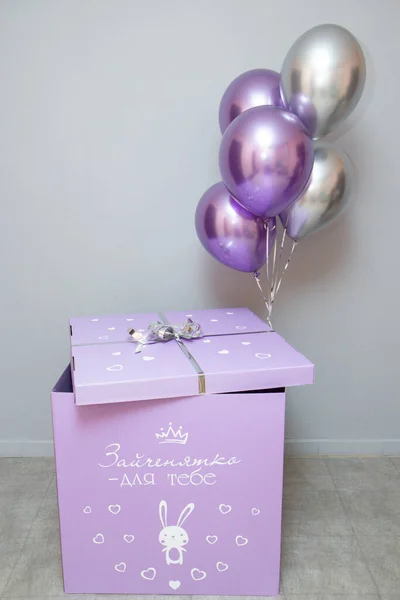 purple box with balloons on the background of the wall, the inscription on the box \