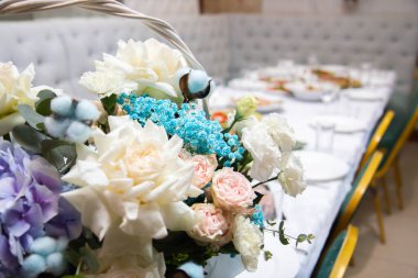 Bir buket bej ve mavi çiçek, arka plandaki sepetin içinde, şenlik masasının üstünde.