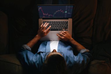 Kanepede dizüstü bilgisayar monitörüne bakan genç iş adamı analisti, indeksleri analiz eden yatırımcı broker, kripto döviz borsası grafiğinde online yatırım verileri alışverişi yapan finansal tablo. Üst görünüm