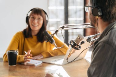 İki genç podcaster kulaklıkla stüdyoda yayın ve kayıt yapıyor. Kadın ve erkek canlı yayın yapıyor, mikrofon kullanarak radyo programlarını yönetiyorlar. Mikrofona seçici odaklanma