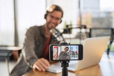 Moda erkek podcast yaratıcısı akıllı telefondan video yayınını kaydediyor. Akıllı telefon kamera ekranına odaklan. Kulaklıklı ve gözlüklü adam podcaster vlog oynatıcısı kanalı için canlı video çekiyor.