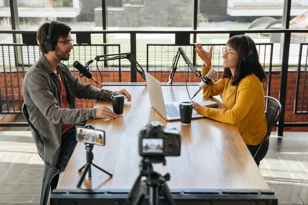 İki genç blogcu, kulaklıklı adam ve kadın konuşurken birbirlerine bakıyorlar, konuşmaları kaydediyorlar, video blogu için röportaj yapıyorlar. Kadın sunucu video podcast 'i için röportaj yapıyor.