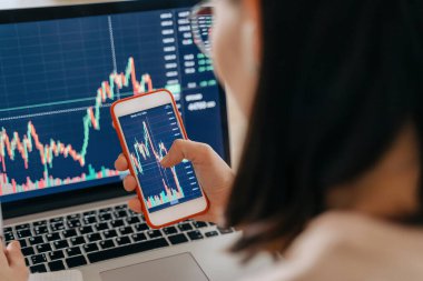 Kadın borsa yatırımcısı analistinin elinde akıllı telefon yatırım uygulama endeksi büyüme grafiği var. Kripto para birimi finansal piyasa analizi için dizüstü bilgisayar kullanıyor. Grafik ticareti verilerini analiz ediyor.