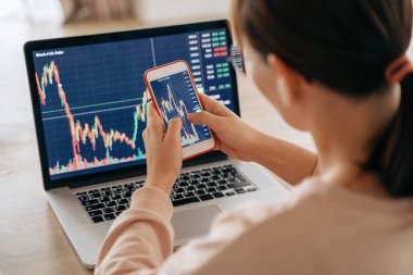 Akıllı telefon uygulaması ve dizüstü bilgisayarı kullanarak kripto para alıp satmak için borsa alım-satımı yapan kadın bir kripto simsarı. Seçici olarak eller ve cep telefonu ekranına odaklan