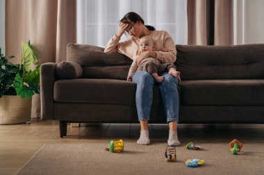 Doğum sonrası depresyon ve stresli annelik kavramı. Yorgun bir kadın baş ağrısı çekiyor. Küçük bebeğini kucağında tutuyor. Uykusuz geceler ve sorunlar yaşıyor. Bekar anne bebeğine tek başına bakar.