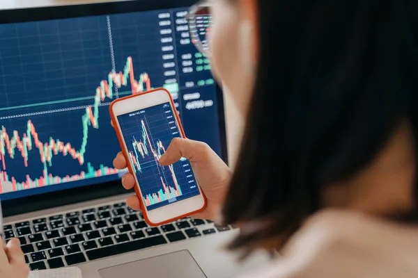 Kadın borsa yatırımcısı analistinin elinde akıllı telefon yatırım uygulama endeksi büyüme grafiği var. Kripto para birimi finansal piyasa analizi için dizüstü bilgisayar kullanıyor. Grafik ticareti verilerini analiz ediyor.