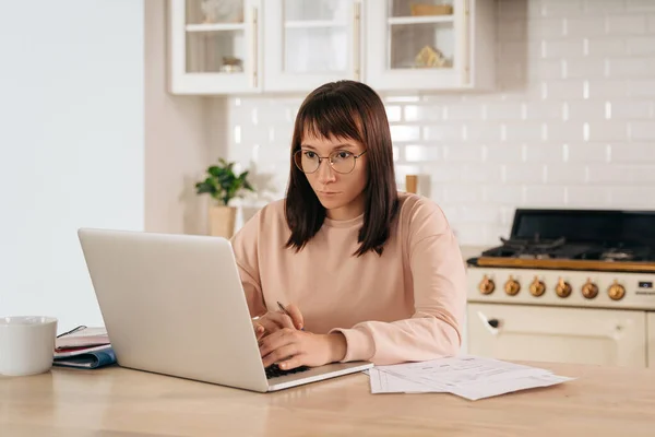 Mulher Séria Usando Óculos Trabalhando Laptop Line Sentado Mesa Cozinha — Fotografia de Stock