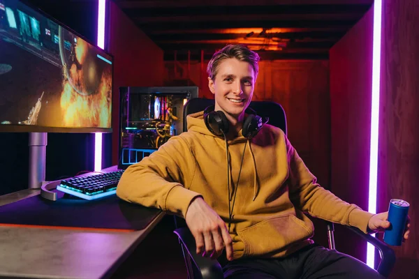 Smiling caucasian pro gamer sitting by gaming setup at home — Fotografia de Stock