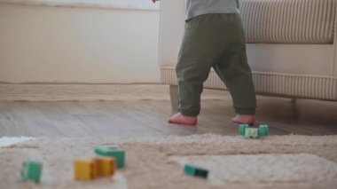 Küçük bebek ayaklarının ilk adımlarını atarken ve oturma odasında yardım almadan yürürken. Küçük çocuk evde yürümeyi öğreniyor. Ağır çekim. Mutlu çocukluk ve çocuğun yeni yetenekleri