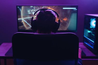 Guy pro gamer playing shooter video game in dark neon coloured room