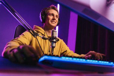 Mikrofon ve kulaklıkla esport turnuvasındaki mutlu profesyonel oyuncu çok oyunculu bir maçın tadını çıkarıyor. Evde bilgisayar oyunu oynayan rekabetçi bir oyuncu. Neon rengi. Sanal spor kavramı