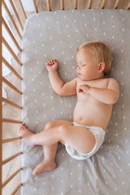 Upper view portrait of little baby boy in diaper lying in his bed napping watching sweet dreams. Safe child sleep. Childcare concept. Happy childhood