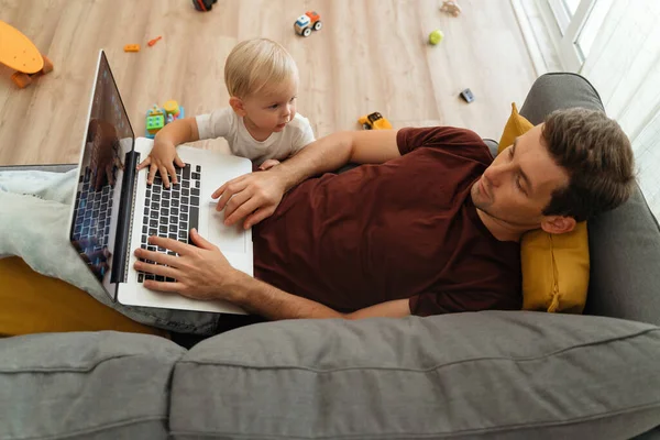 Naughty Little Baby Boy Bothering His Father Lying Couch Laptop — Stockfoto