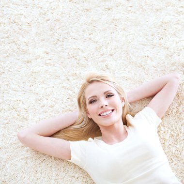 Beautiful blond woman posing lying down on a carpet.