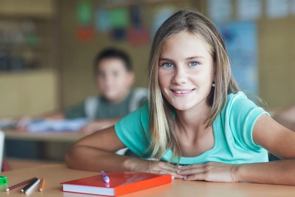 Colegiala sonriente sentada en el aula — Foto de Stock