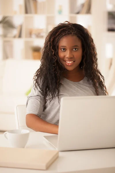 Lachende Afrikaanse tienermeisje laptop thuis gebruiken — Stockfoto