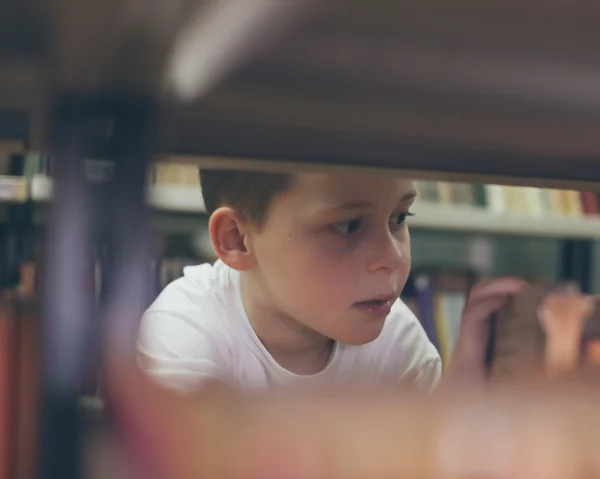 Niño buscando libros en la biblioteca — Foto de Stock