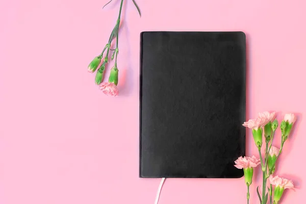 Siyah boş kitap ya da dizüstü bilgisayar ve pastel pembe arkaplan üzerindeki çiçekler için metin için boşluk