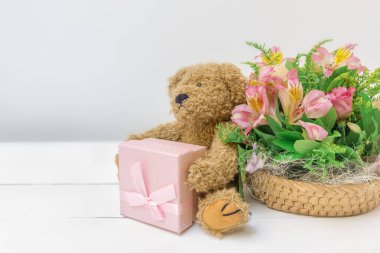 Çiçek buketi, oyuncak ayı ve beyaz arka planda sunulan sevimli bir şenlik arka planı.