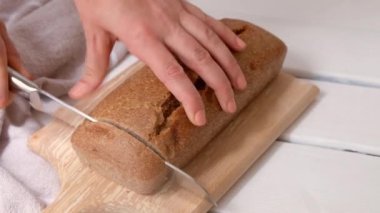 Kadın elleri bıçak tutuyor ve beyaz ahşap arka planda tahtanın üzerinde ev yapımı ekmek kesiyor.