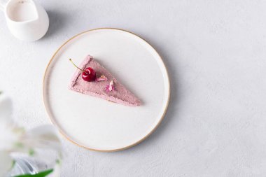Top view of a slice of a raw cherry cake on white plate on a neutral grey background. Healthy raw dessert