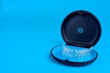 Black plastic case with transparent braces on blue background. Insivible removable retainers for orthodontic treatment clipart