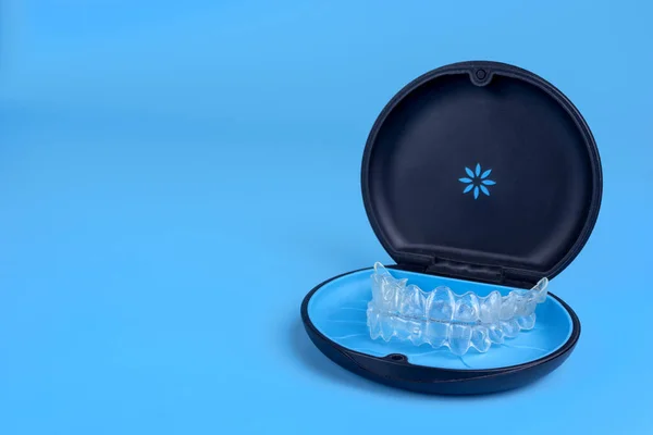 Black plastic case with transparent braces on blue background. Insivible removable retainers for orthodontic treatment — Stock Photo, Image