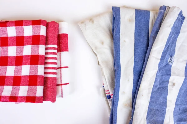 Three new red checkered kitchen picnic towels folded versus old dirty torn blue cloth towels. Cleaning and regularly changing kitchen rags and cloth.