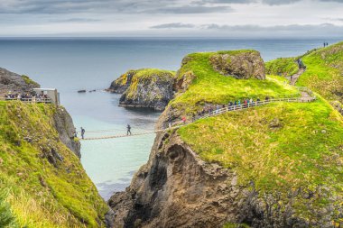 İnsanlar Kuzey İrlanda 'daki adaya ulaşmak için Carrick' e bir ip köprüsünü geçmek için kuyruğa giriyorlar.