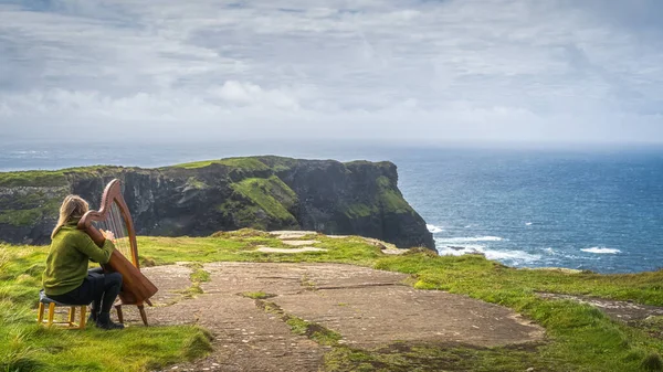 Mujer tocando el arpa en la cima de los icónicos Acantilados de Moher, Irlanda Imagen de archivo