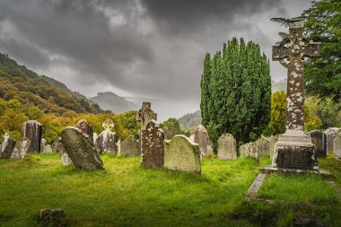 Wicklow, İrlanda, Ağustos 2019 Glendalough Mezarlığı 'nda Kelt haçları olan antik mezarlar dağlar ve arka planda dramatik fırtına gökyüzü