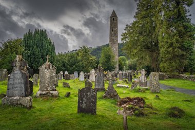 Wicklow, İrlanda, Ağustos 2019 Ortaçağ Kulesi ve Glendalough Mezarlığı 'nda Kelt haçları olan antik mezarlar. Arka planda kasvetli fırtına gökyüzü