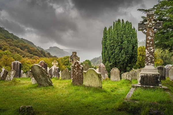 2019年8月 爱尔兰威克洛 位于格伦达洛夫公墓的带有凯尔特十字的古老坟墓 背景为山脉和戏剧性的风暴天 — 图库照片