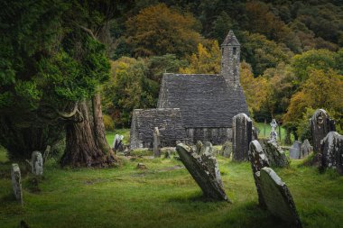 Ortaçağ kilisesi, antik mezarlar, Glendalough Mezarlığı 'nda Kelt haçları sonbahar ormanı ve arka planda dağlar, Wicklow, İrlanda