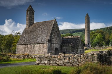 Ortaçağ kilisesi, antik mezarlar, Glendalough Mezarlığı 'ndaki Kelt haçları, arka planda orman ve dağlar, Wicklow, İrlanda